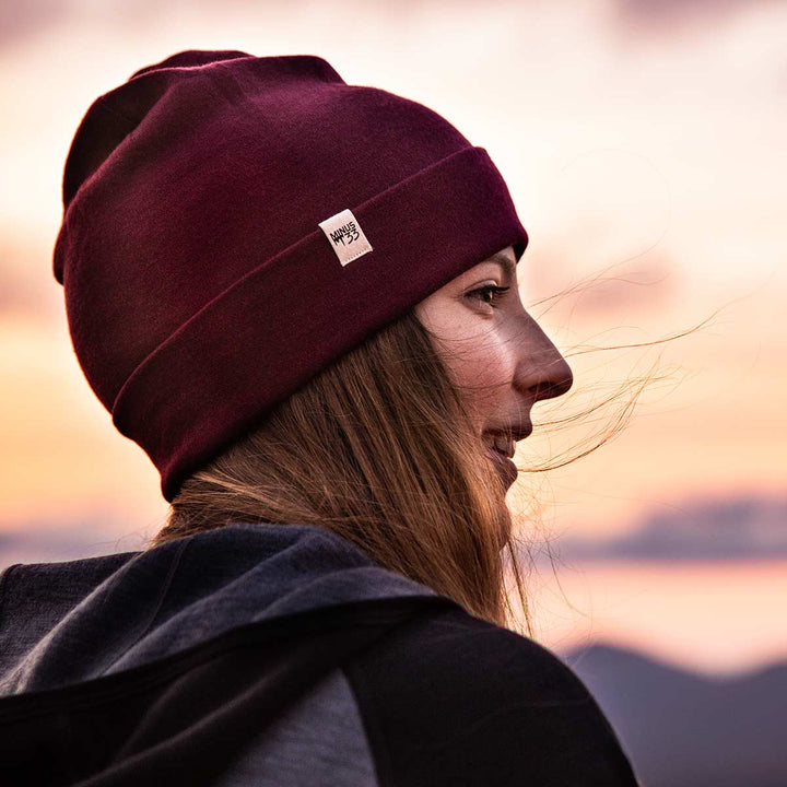A woman watching the sunset models a lightweight, double-layered, hundred percent, super soft merino wool beanie with a midweight wool hoodie. This hat is perfect for a hike up the mountain or a walk around the block!
#color_burgundy