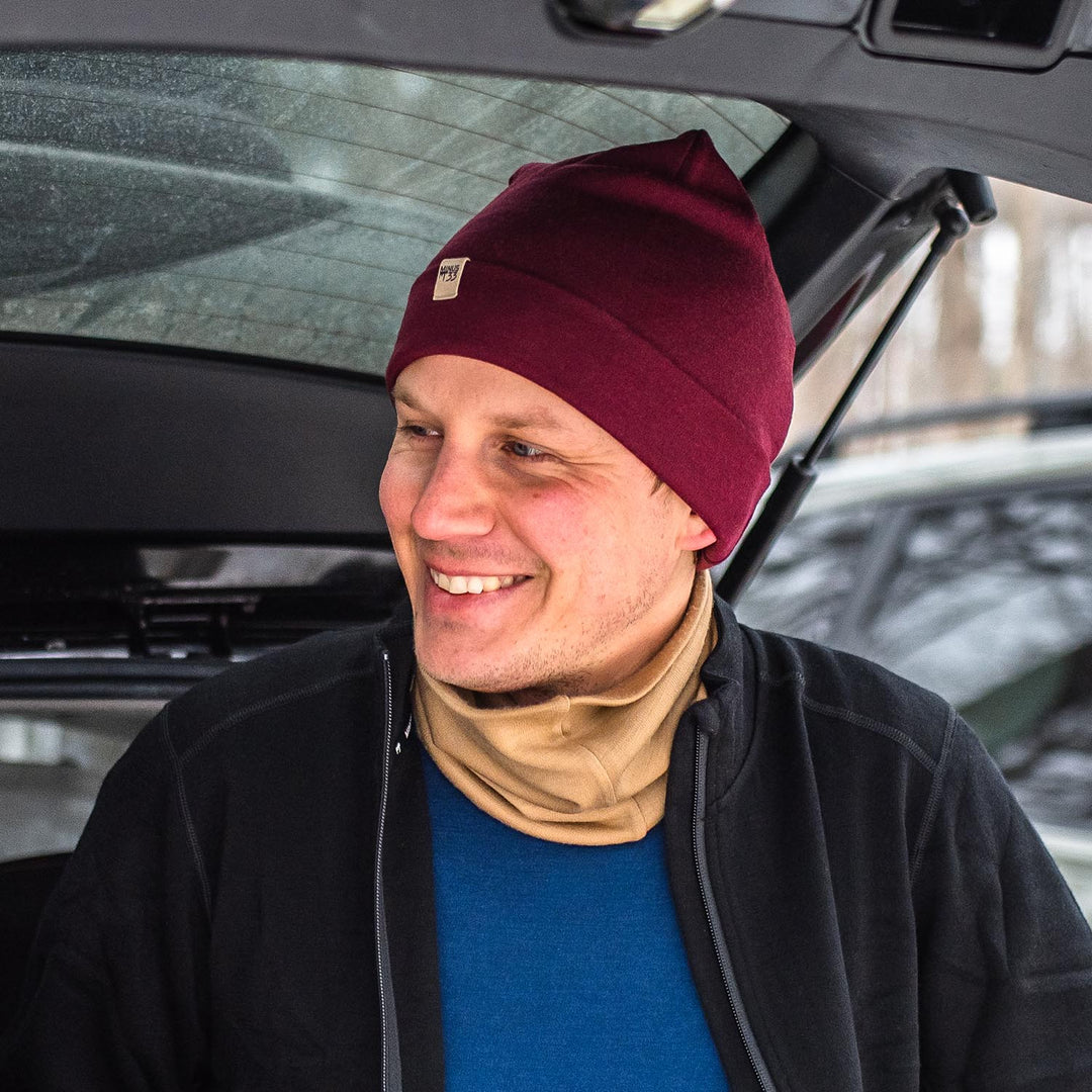 A man models a lightweight, double-layered, hundred percent, super soft merino wool beanie with a midweight wool neck gaiter, midweight base layer, and heavyweight zip-up sweater. This hat is perfect for a hike up the mountain or a walk around the block!
#color_burgundy