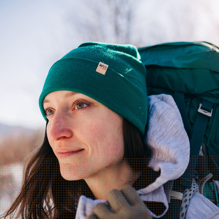 A woman models a lightweight, double-layered, hundred percent, super soft merino wool beanie with our heavyweight brushed wool hoodie on a winter trail. This hat is perfect for a hike up the mountain or a walk around the block!
#color_emerald-green