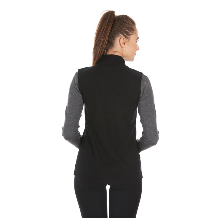 A woman models a hundred percent merino wool heavyweight full zip vest. This outer layer features a two and a half inch mock neck collar and two zippered pockets. #color_black