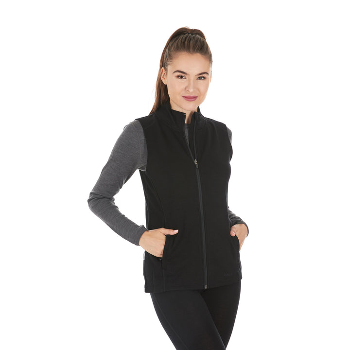 A woman models a hundred percent merino wool heavyweight full zip vest. This outer layer features a two and a half inch mock neck collar and two zippered pockets. #color_black