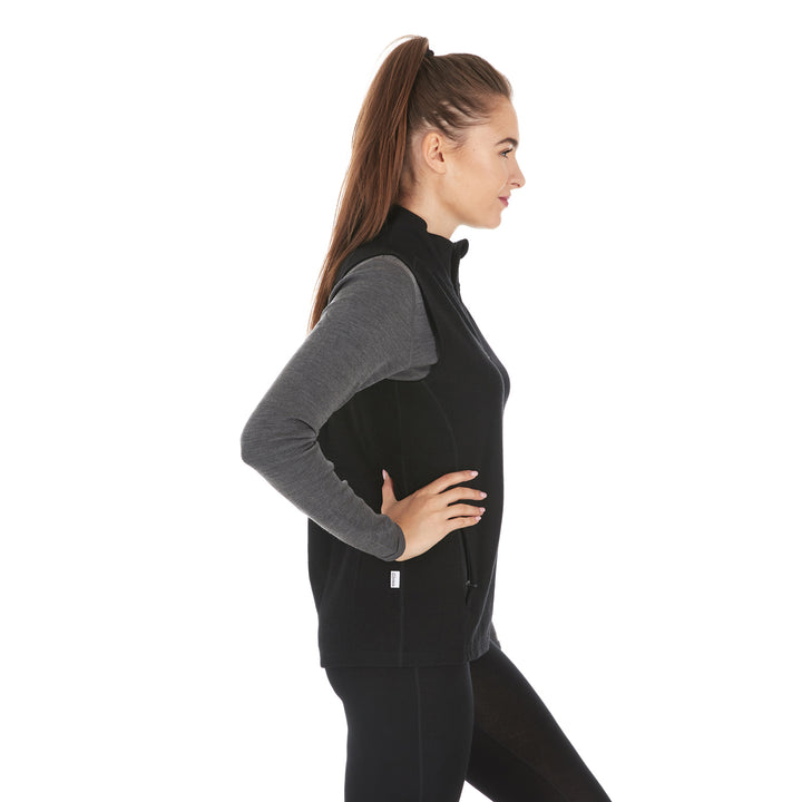 A woman models a hundred percent merino wool heavyweight full zip vest. This outer layer features a two and a half inch mock neck collar and two zippered pockets. #color_black