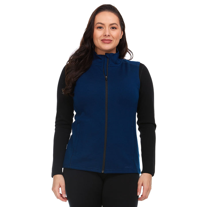 A woman models a hundred percent merino wool heavyweight full zip vest. This outer layer features a two and a half inch mock neck collar and two zippered pockets. #color_navy